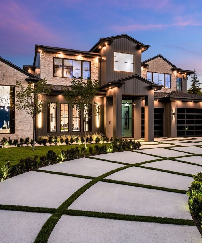 Modern luxury home exterior with a beautifully landscaped front yard and driveway at dusk.